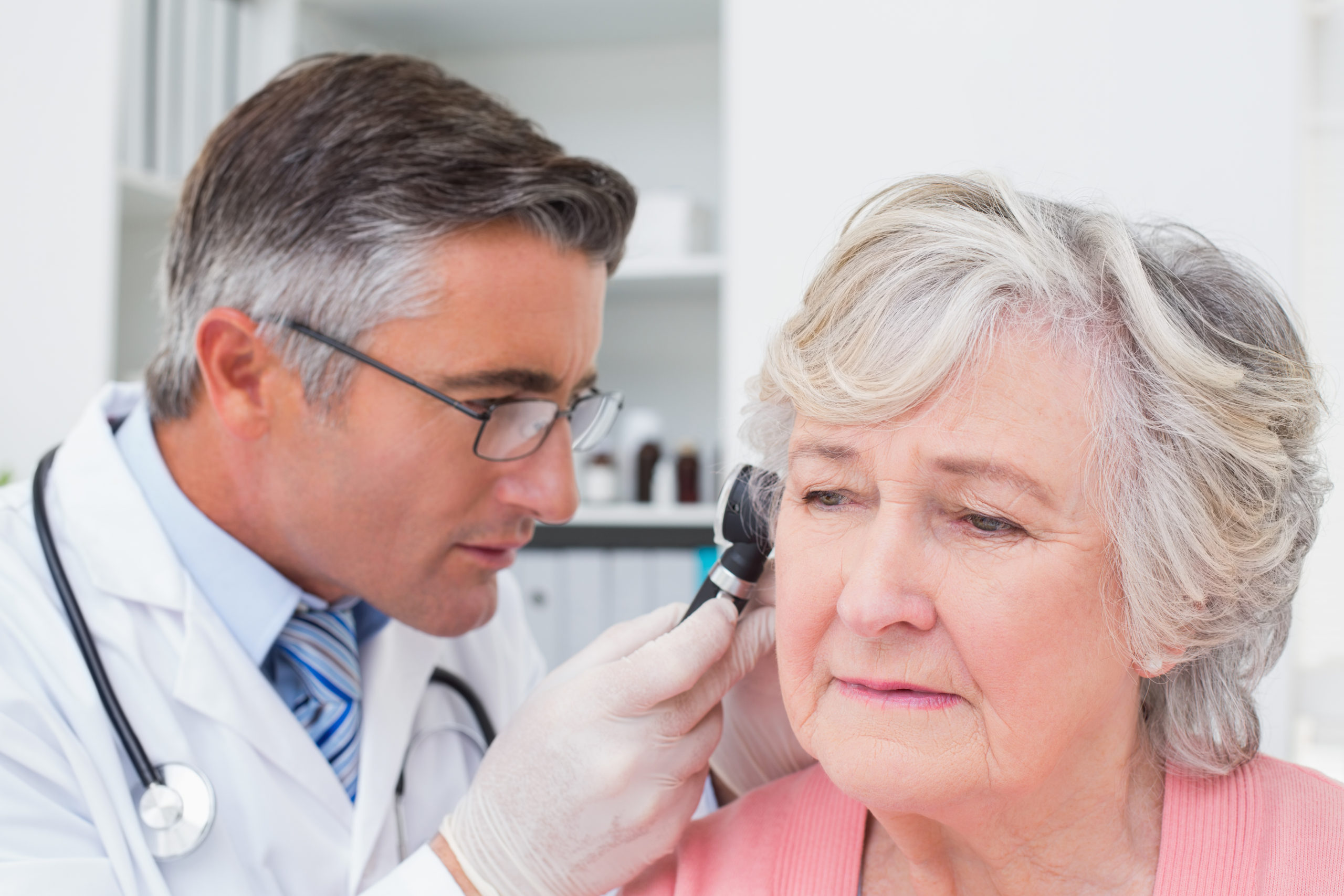 Male doctor examining female patients ear with otoscope in clinic
